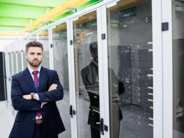 A professional IT administrator standing in a server room managing business network infrastructure.