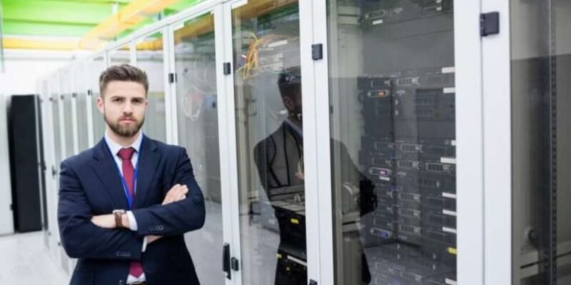 A professional IT administrator standing in a server room managing business network infrastructure.